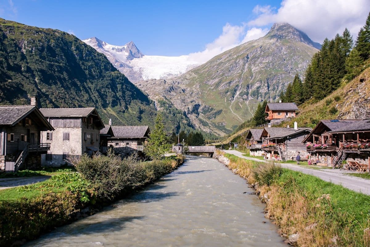Village alpin de montagne avec chalets en bois le long d'une rivière et sommets enneigés des Alpes en arrière-plan, contexte local des Hautes-Alpes